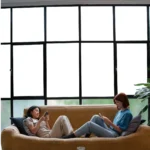 Two people relaxing on a sofa in front of large smart glass windows in opaque mode, showcasing privacy and comfort.