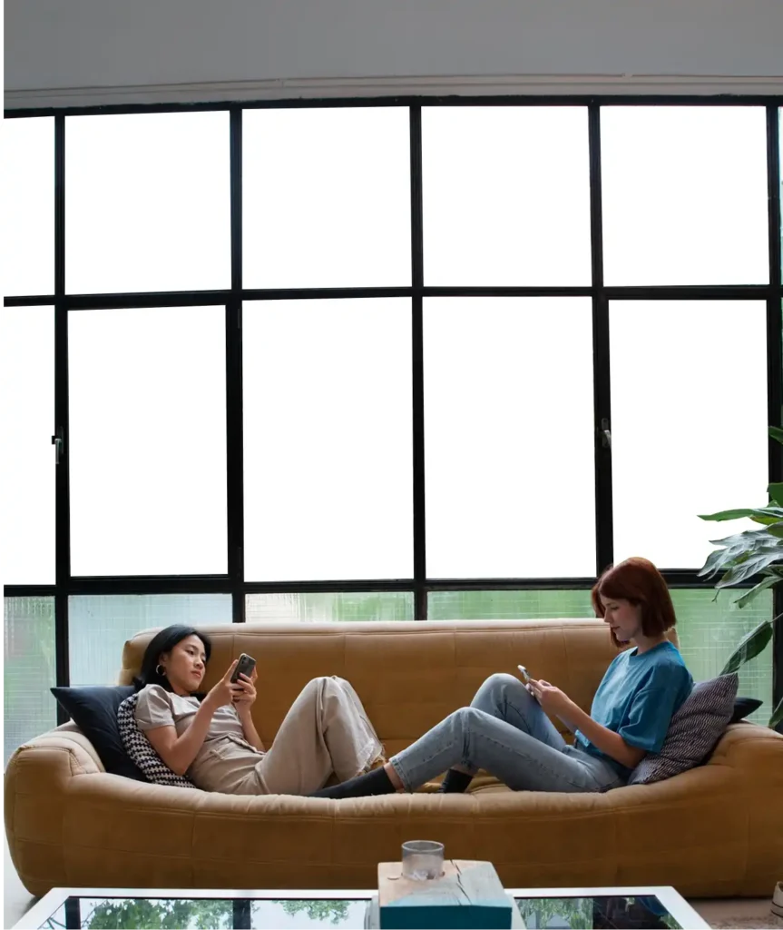 Two people relaxing on a sofa in front of large smart glass windows in opaque mode, showcasing privacy and comfort.